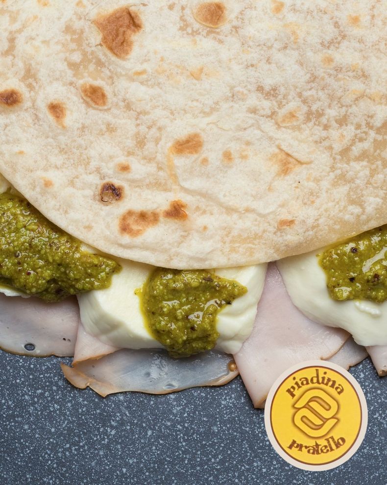 Piatto con tortilla farcita con carne a fette, formaggio fuso e salsa al pesto verde.