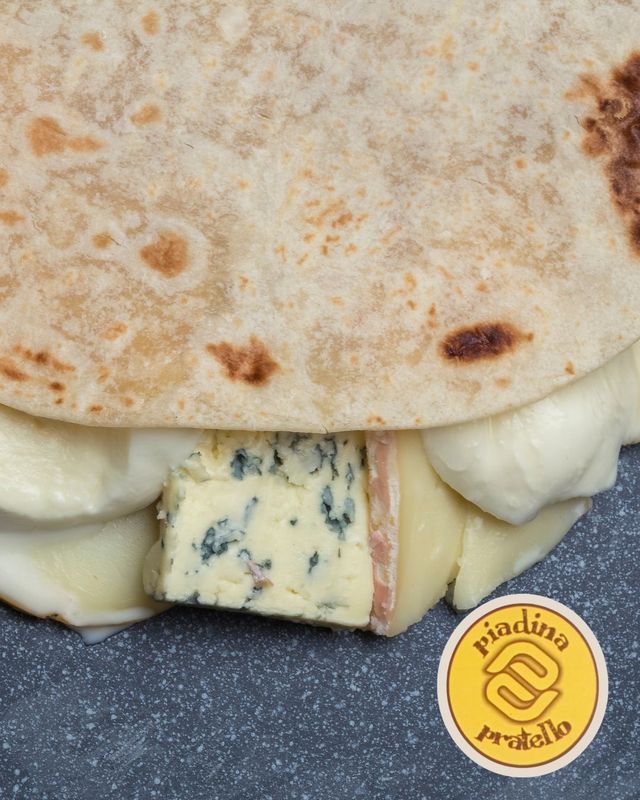 Primo piano di un panino con formaggio e pane piatto, ripieno di gorgonzola, su un piatto scuro.