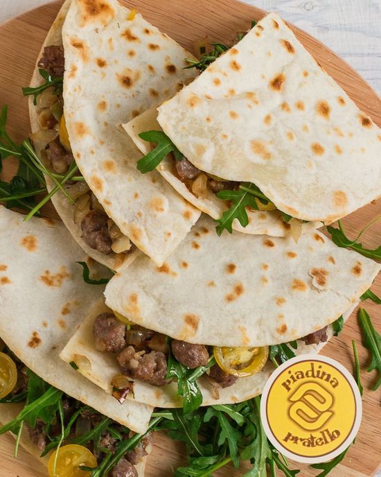 Pila di focacce piegate con carne e verdure su un piatto di legno, sormontate da un piccolo adesivo con il logo.