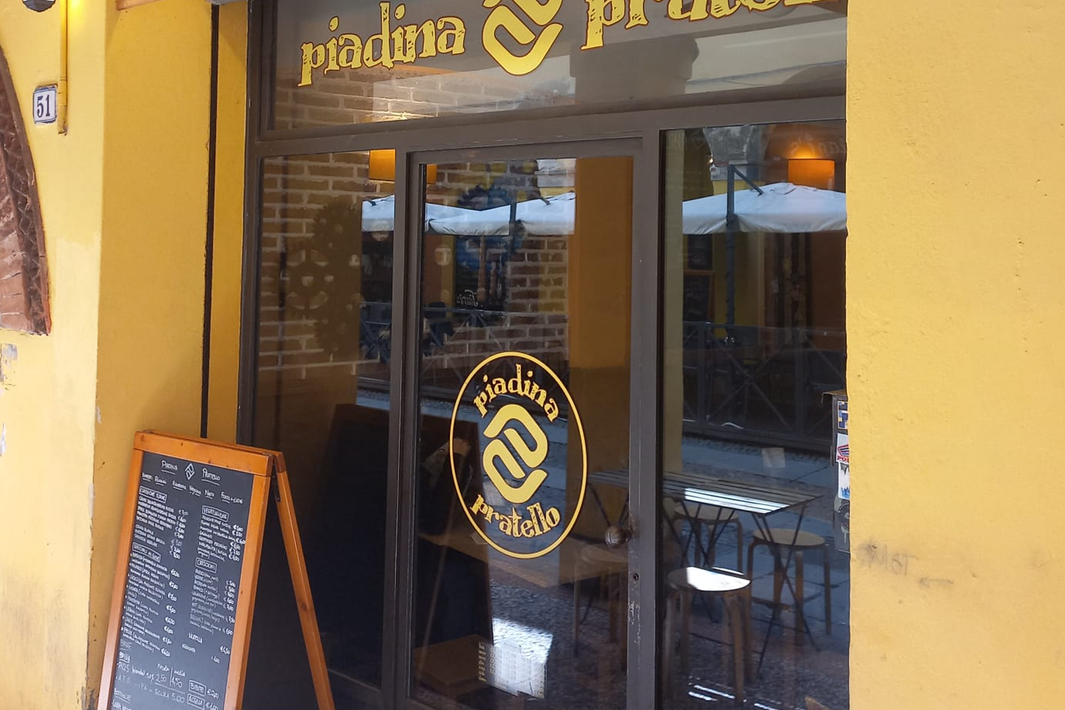 Vetrina gialla con porta a vetri, logo del bar e menù scritto su una lavagna sul marciapiede.