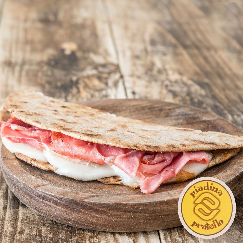 Panino con focaccia, formaggio fuso e prosciutto su un tagliere di legno, con uno sfondo rustico.