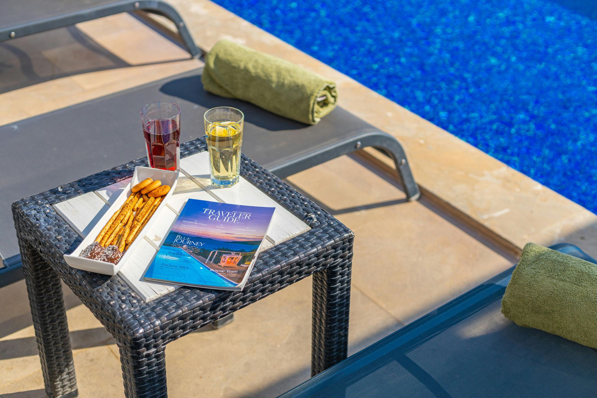 Poolside table with drinks, magazines, and towels beside a blue swimming pool