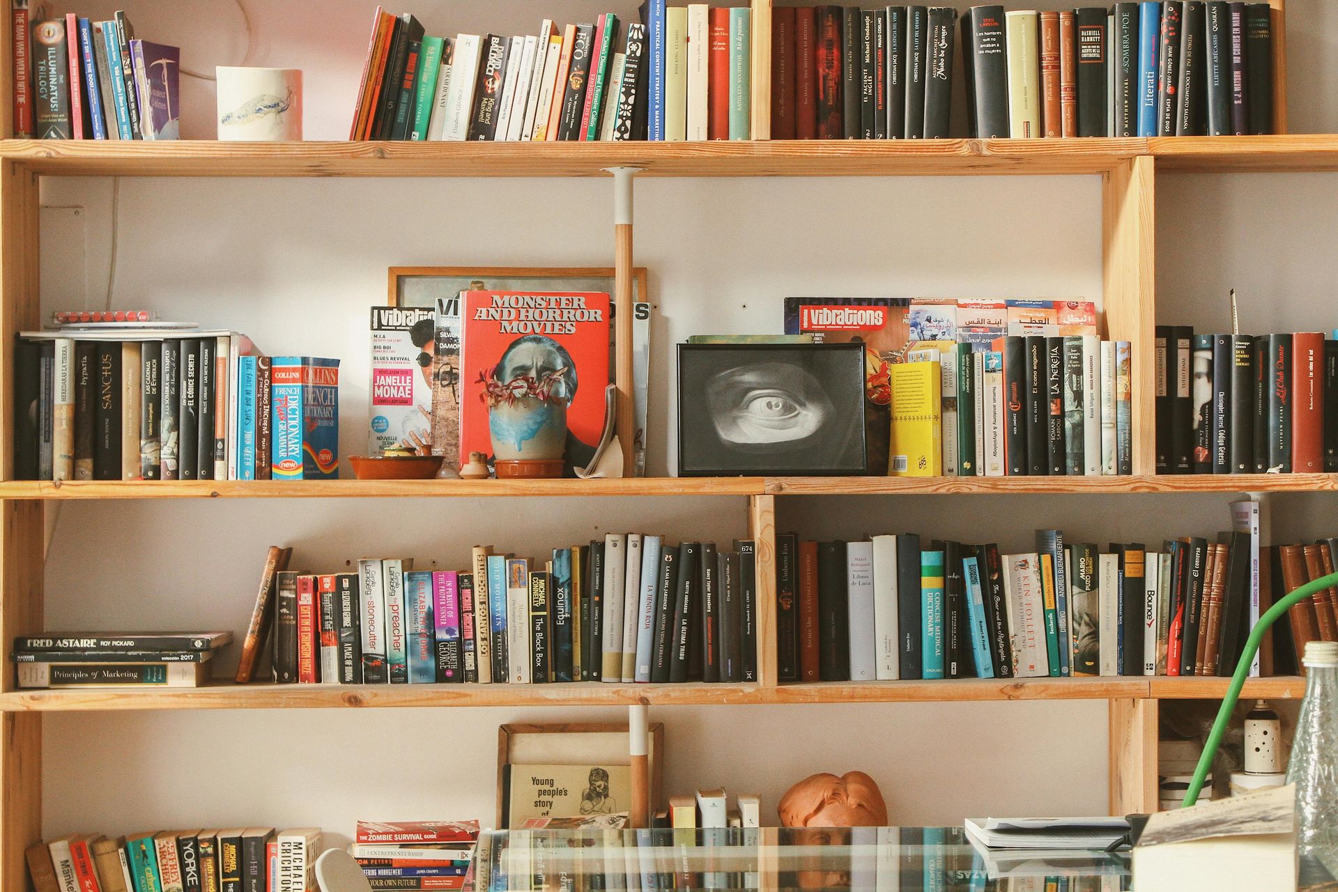Wooden bookshelf filled with books, with a small framed photo and a green lamp on the right.