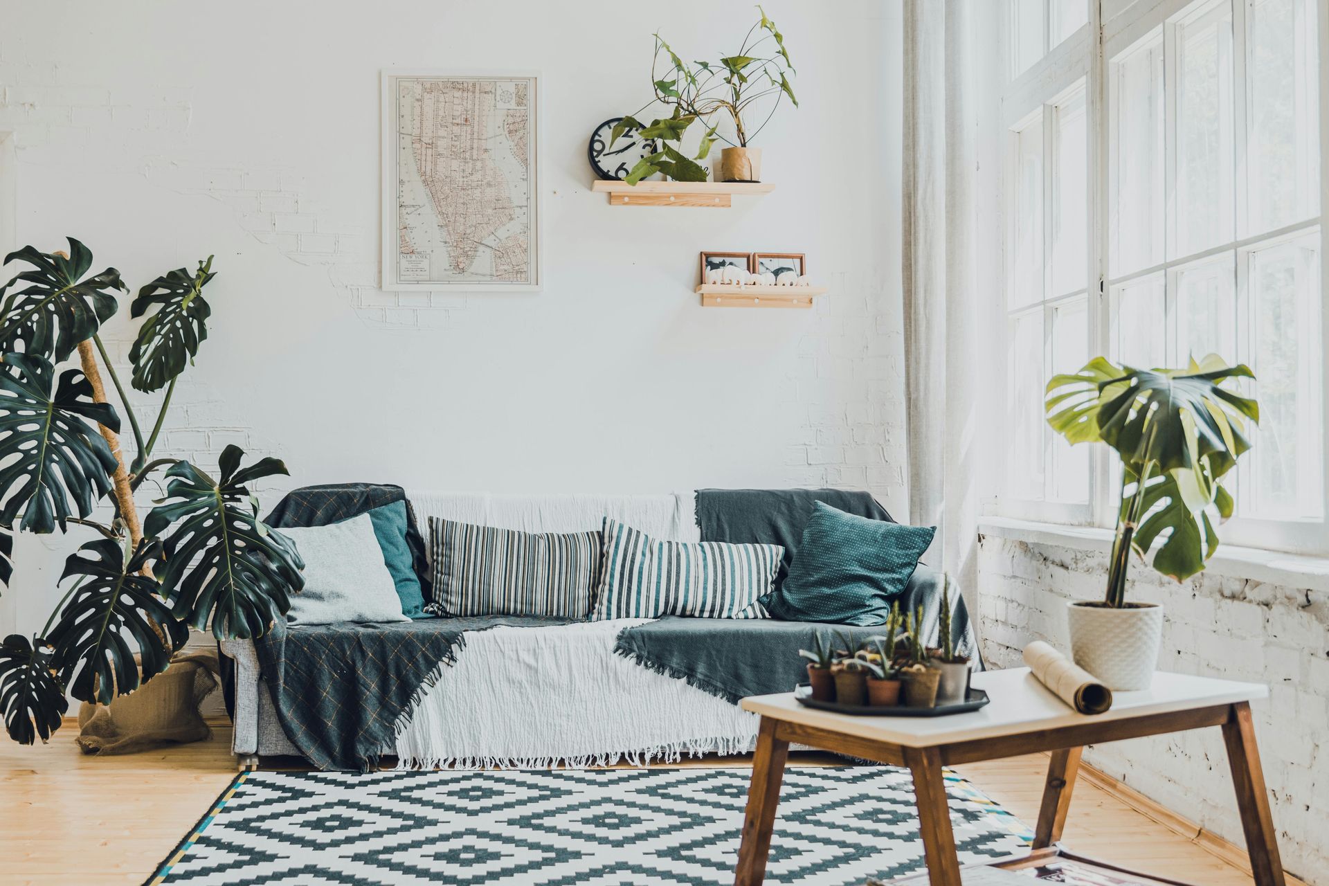 Bright living room with teal sofa, patterned rug, wooden coffee table, and large sunlit windows
