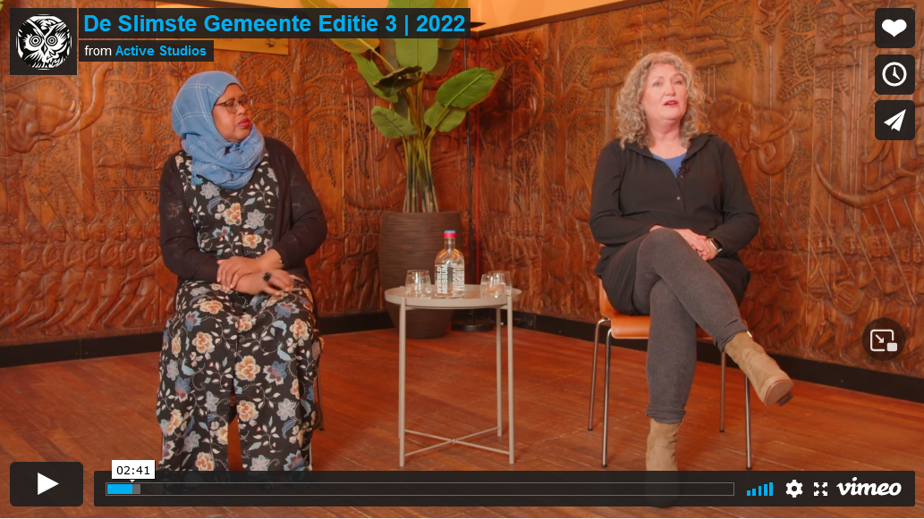 Twee vrouwen zitten in een studio te overleggen. De ene draagt een hijab en een jurk met bloemenprint, de andere een donkere top en een grijze broek.