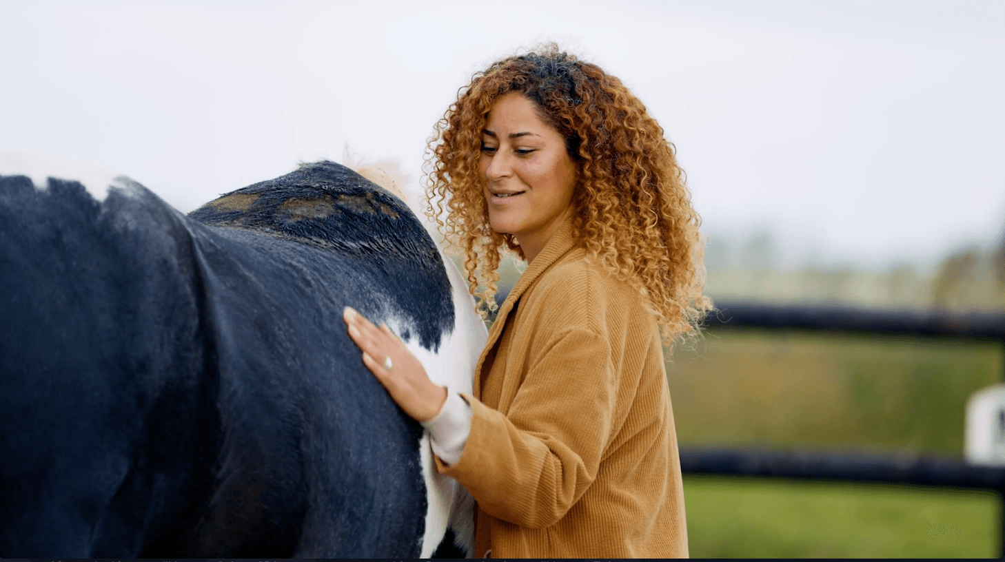 Vrouw aait een zwart-wit paard in de buitenlucht; lacht, bruine jas.