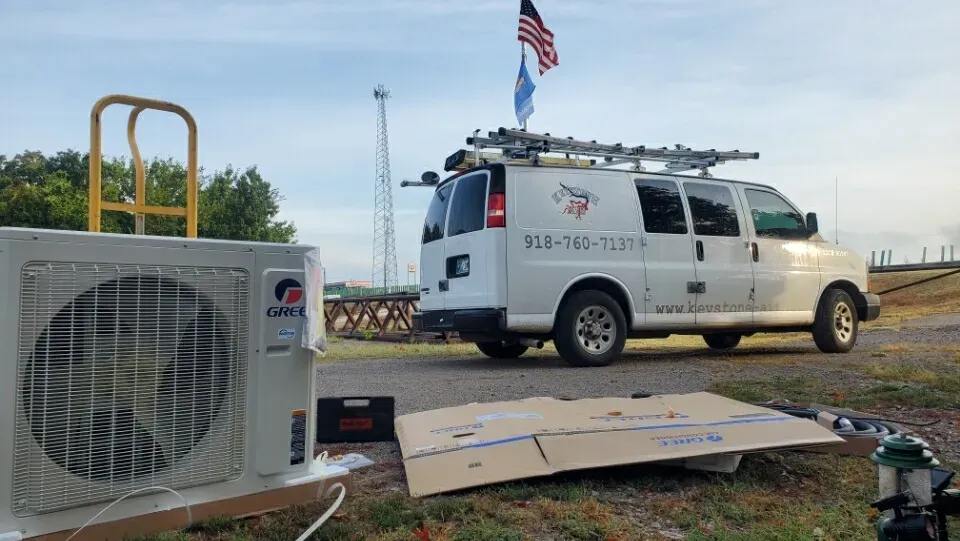 White utility van beside a portable air conditioner unit and scattered cardboard in an outdoor work area.