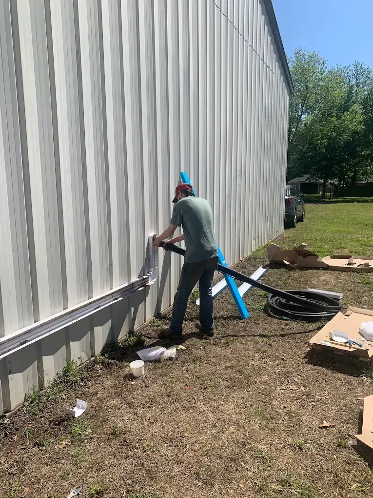 Worker in a blue hard hat painting the side of a metal building outdoors