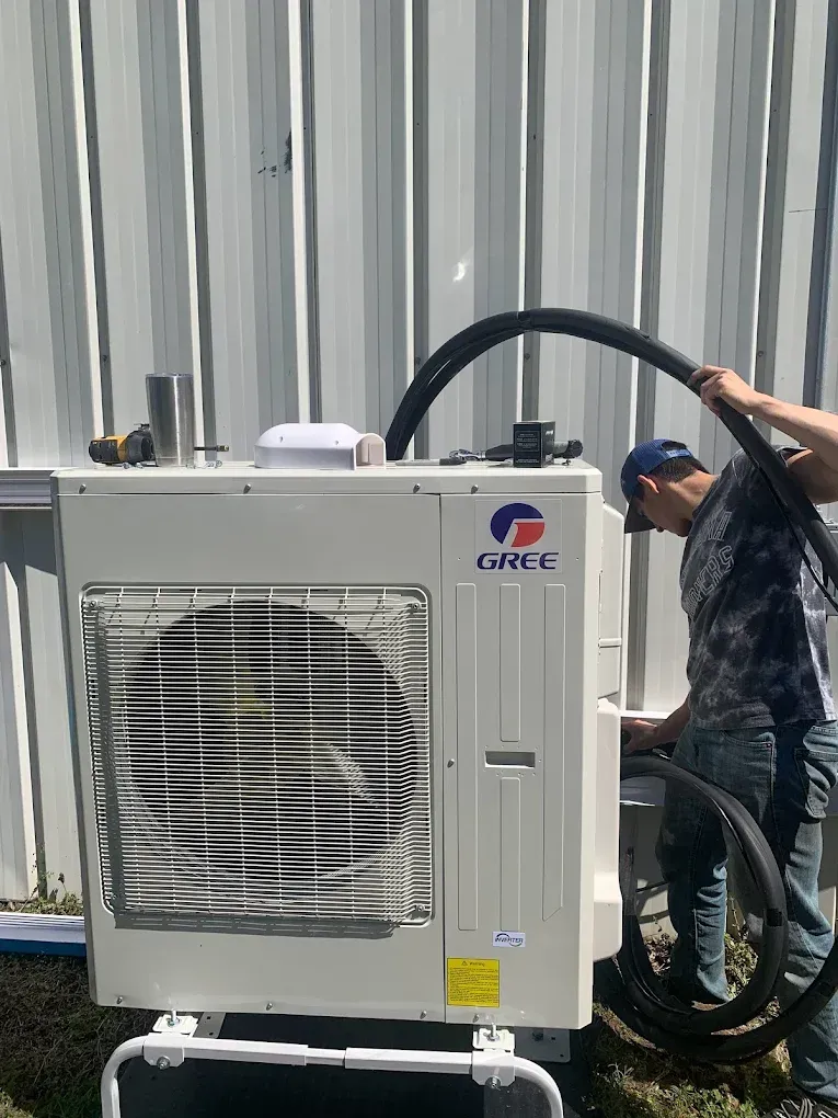 Outdoor air conditioner unit being serviced by a technician beside a corrugated metal wall.