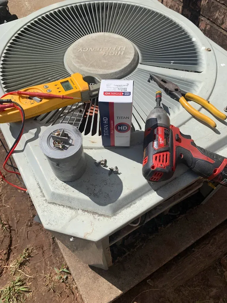 Tools laid out on an outdoor HVAC unit, including a drill, tester, pliers, and a wiring component.