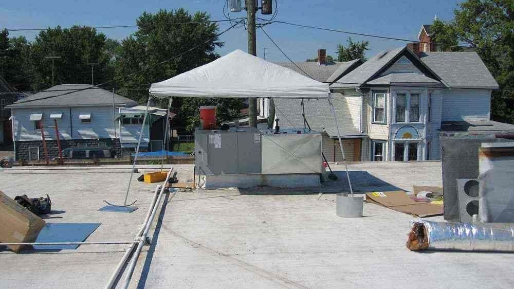 Rooftop scene with a white canopy sheltering HVAC equipment. Buildings and sky in the background.