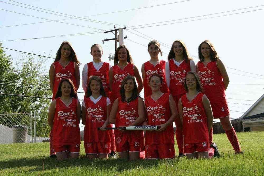 Softball team in red uniforms poses outdoors on a sunny day, holding a bat.