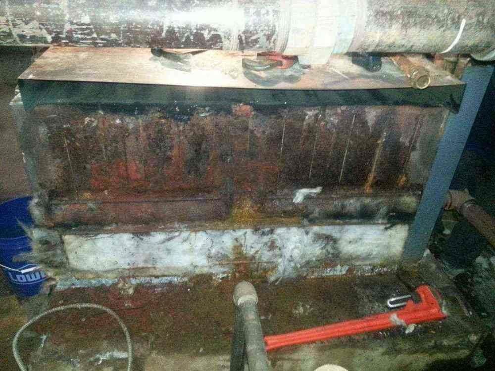 Rusty boiler with water damage and tools on the floor.