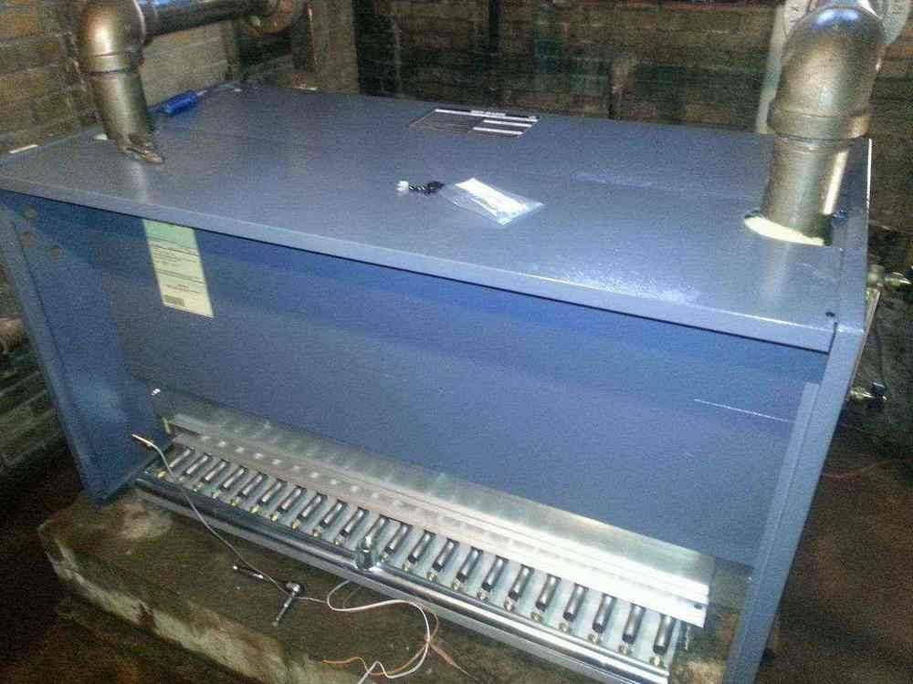 Blue heating unit with pipes, in a basement setting.