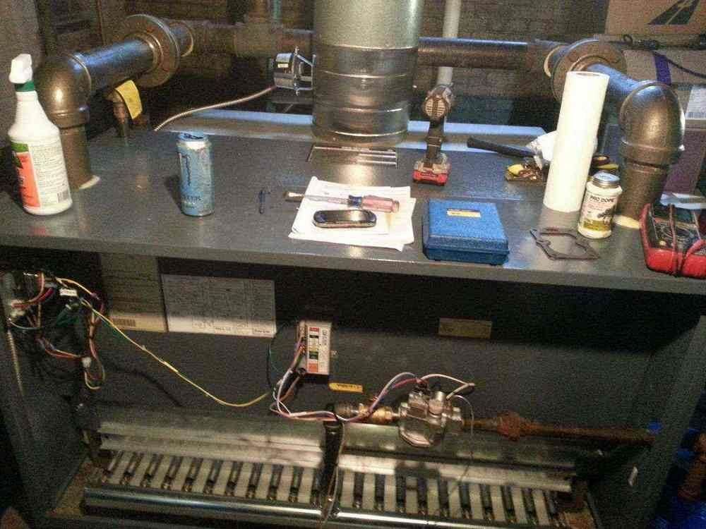 Furnace interior with tools on top: pipes, wiring, burner, metal surface, and various bottles and containers.