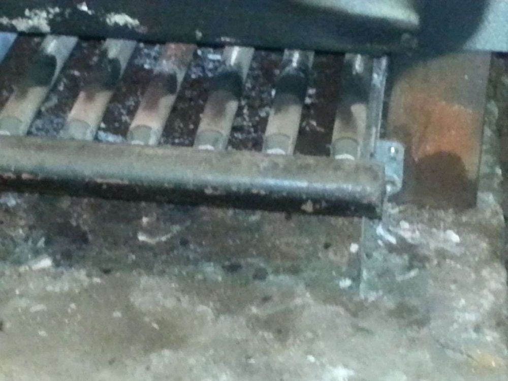 Close-up of a furnace burner. Gray metal burners are covered in ash, in a dark, dusty setting.