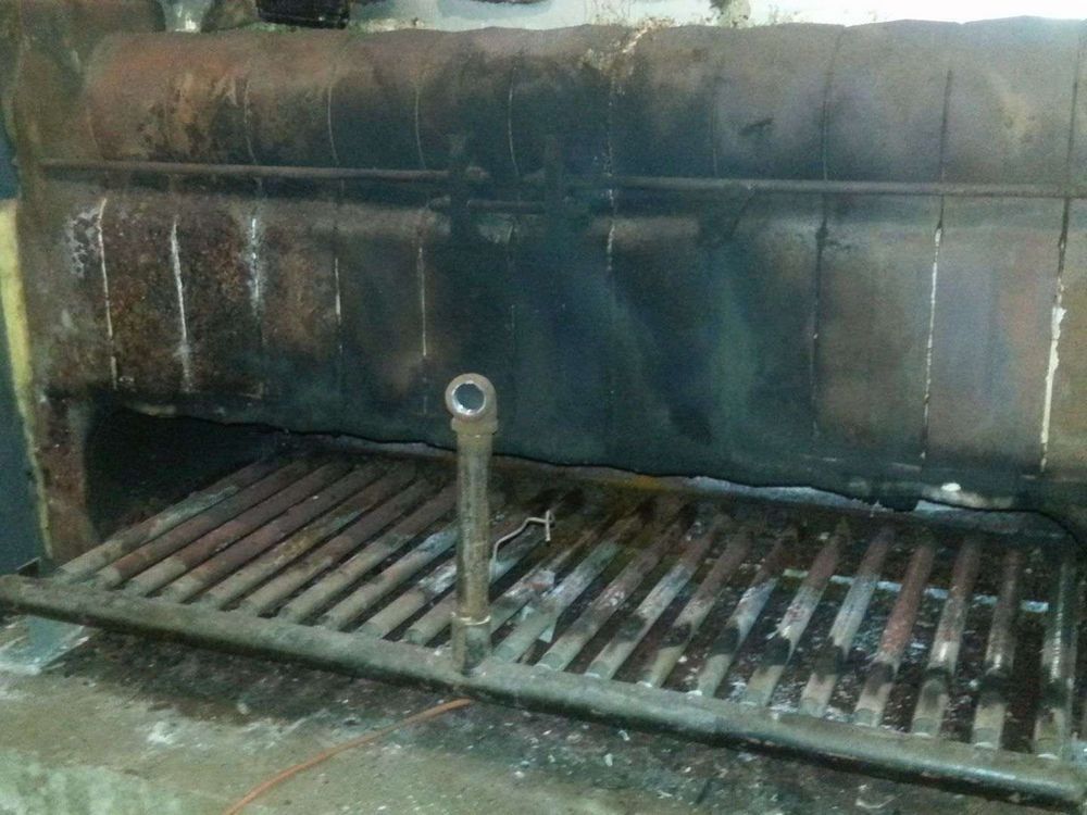 Interior of a dirty industrial oven with a metal grate and a central metal pipe.