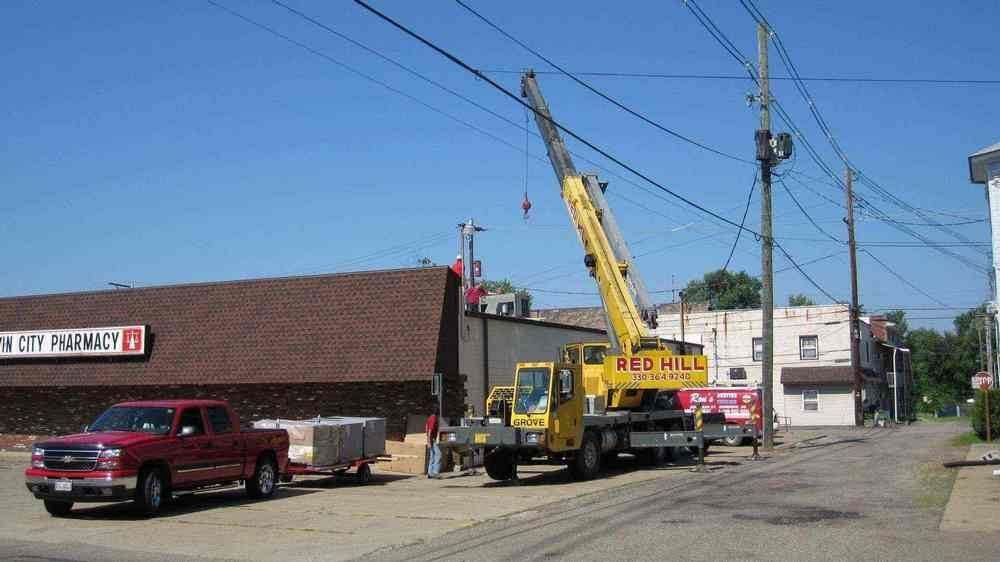 A yellow crane working near power lines in a town street. A red pickup truck and a building are also present.