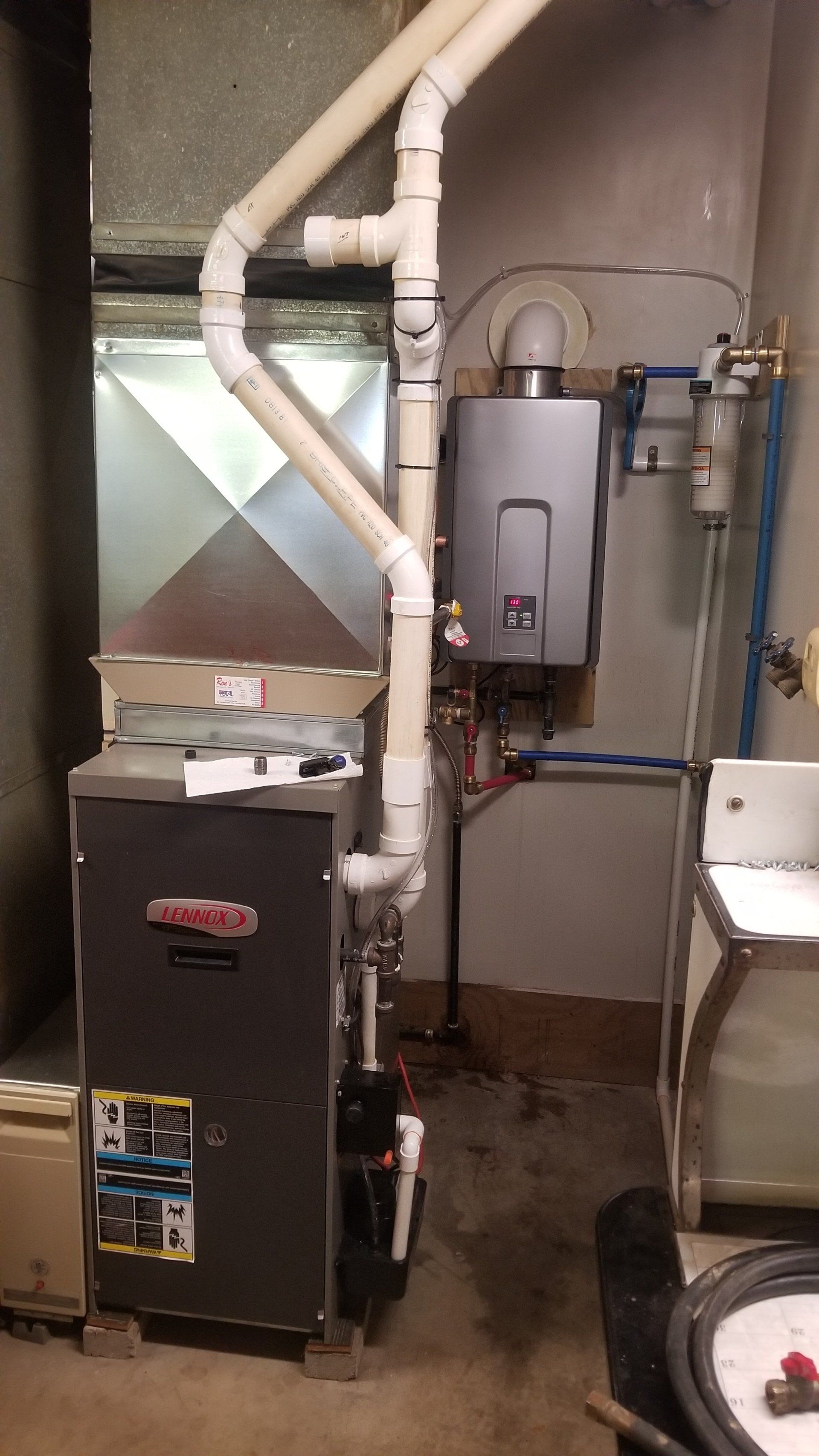 Furnace and water heater in a basement laundry room. White pipes, metal appliances against a concrete wall.