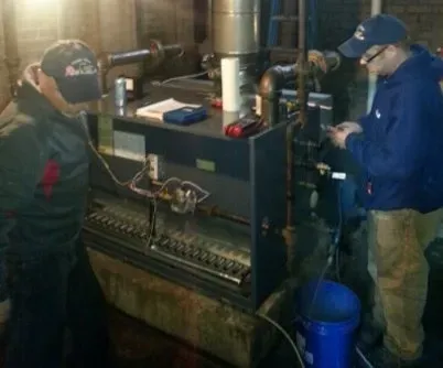 Heating System Installation — Dennison, OH — Ron’s Heating & Cooling Two men in a basement examining a furnace. One uses a tool, the other consults a device.