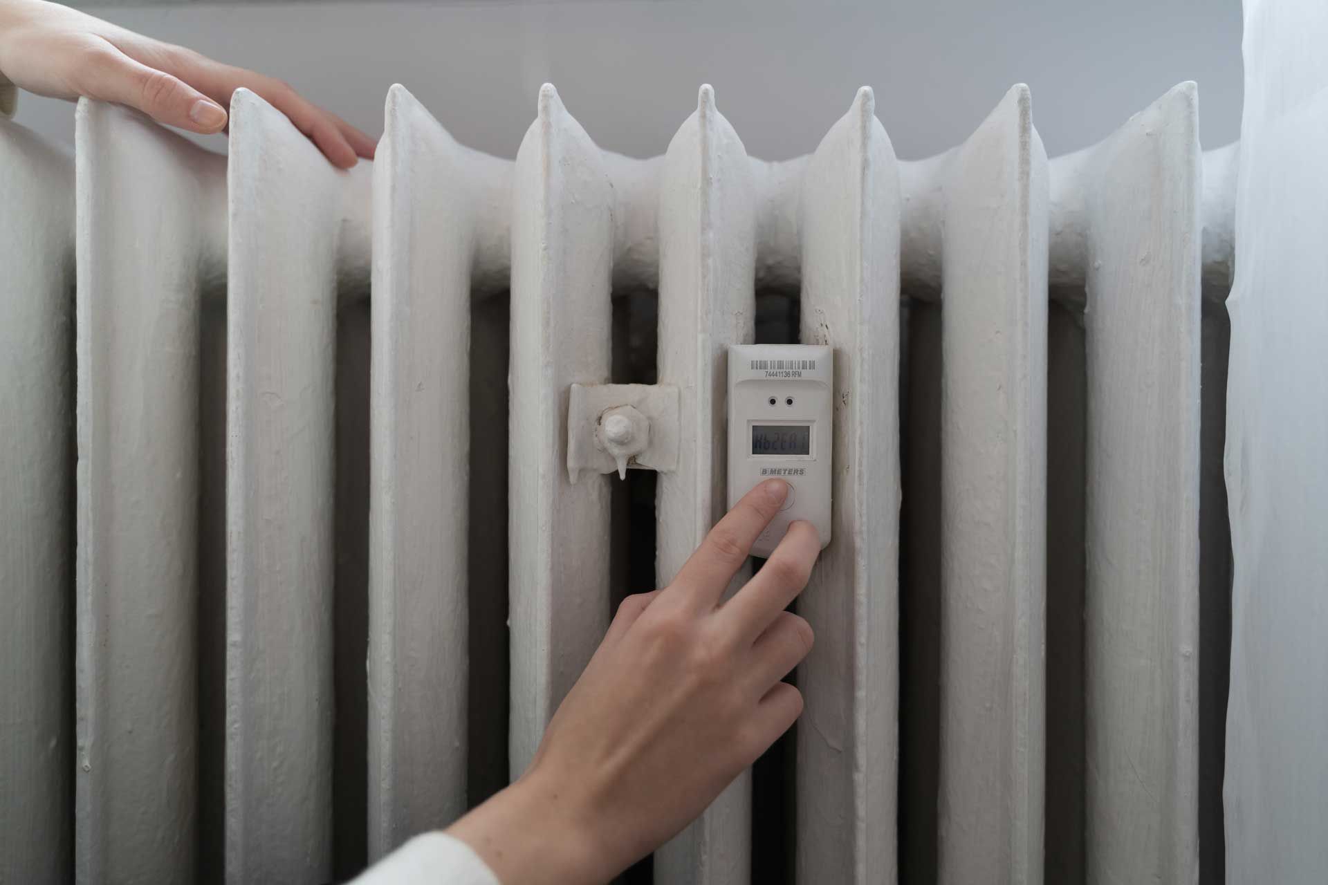 Hands adjusting a thermostat on a white radiator.