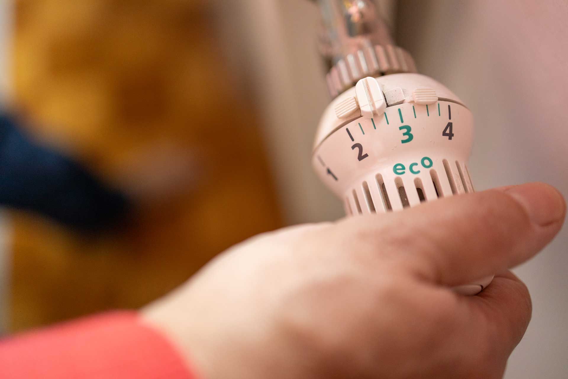 Hand adjusting a radiator thermostat, marked with numbers and an 