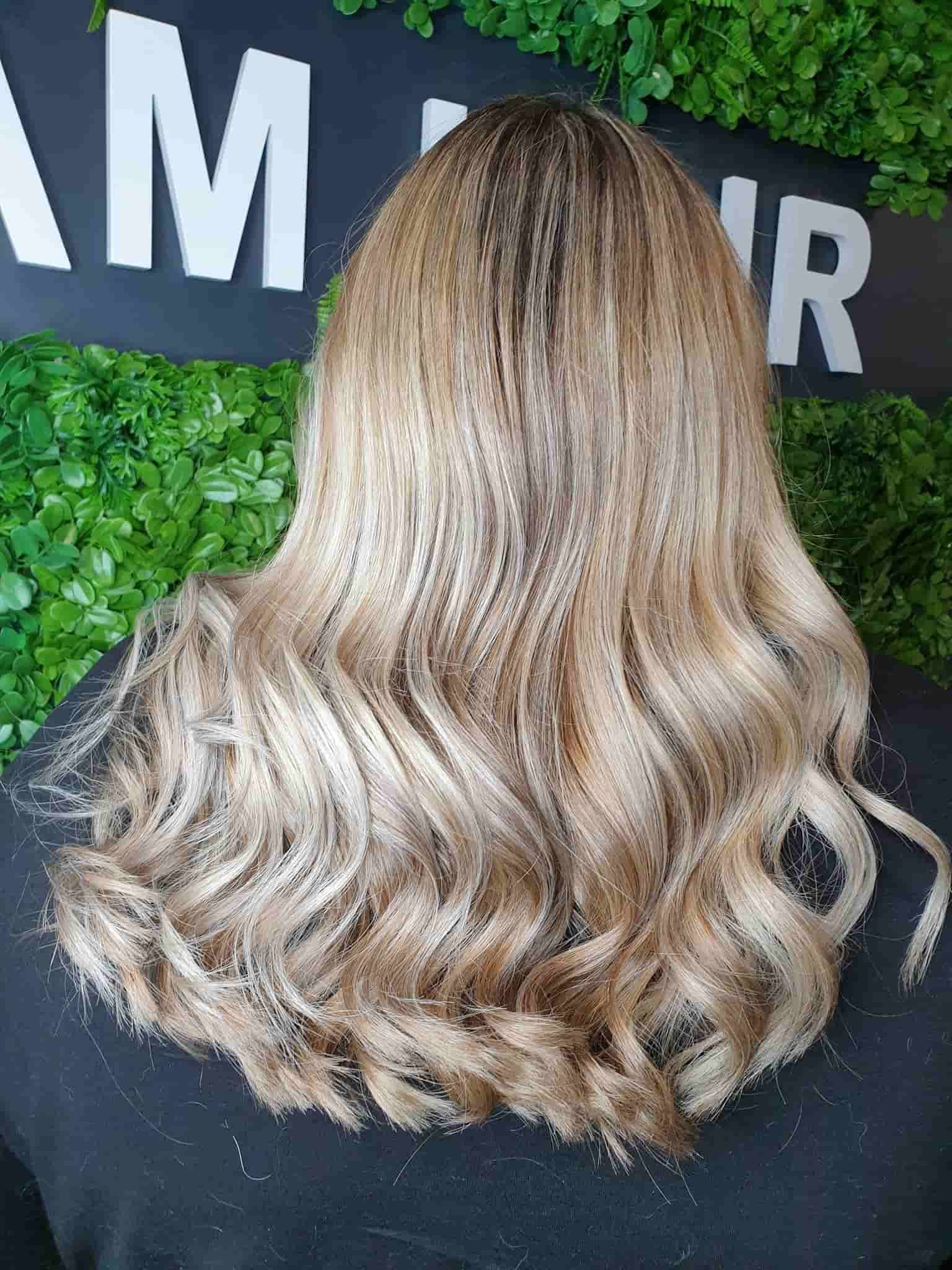 A woman with long blonde hair is standing in front of a sign — Glam Hair and Beauty in Woy Woy, NSW