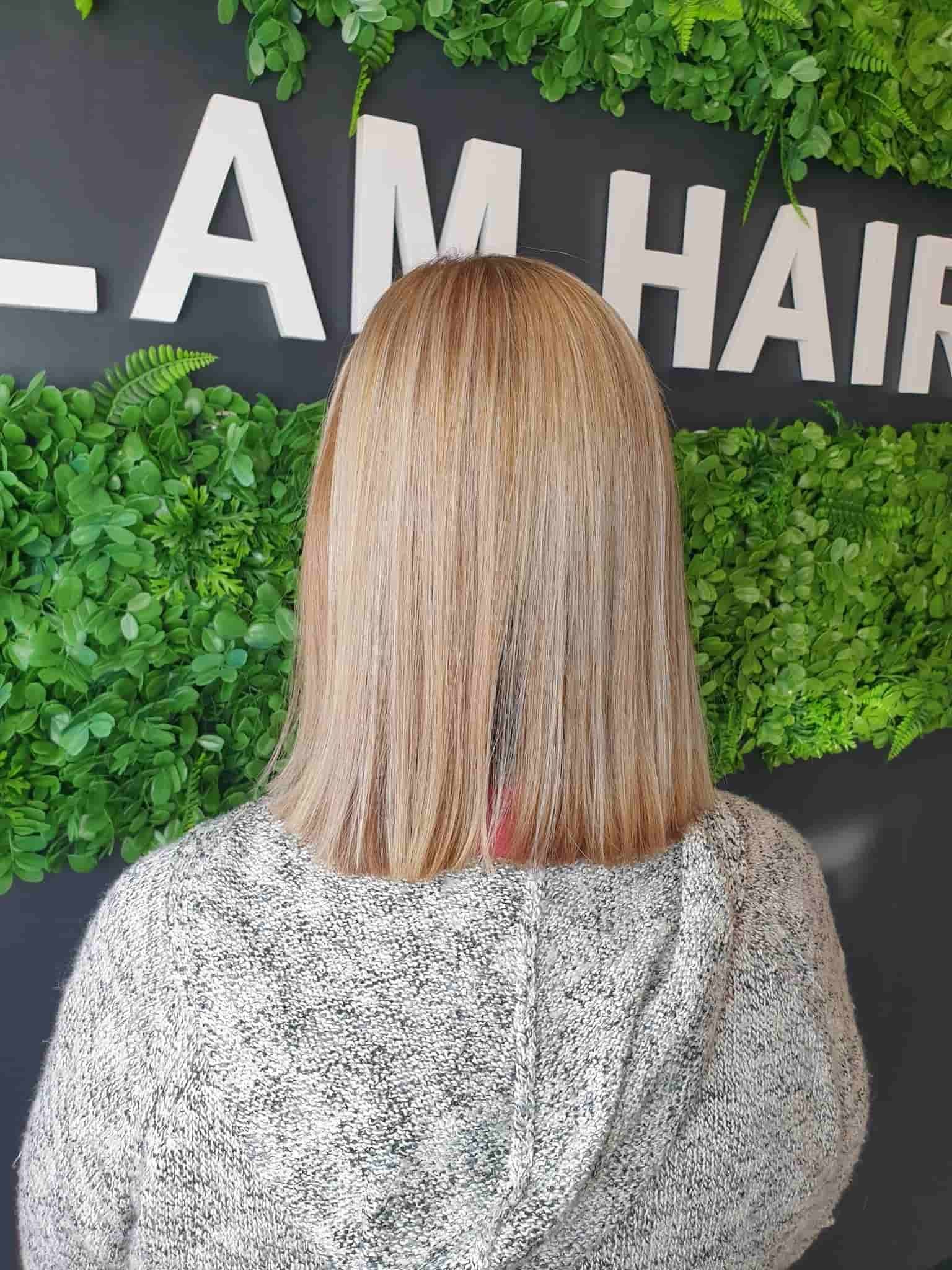 A woman with blonde hair is standing in front of a sign — Glam Hair and Beauty in Woy Woy, NSW
