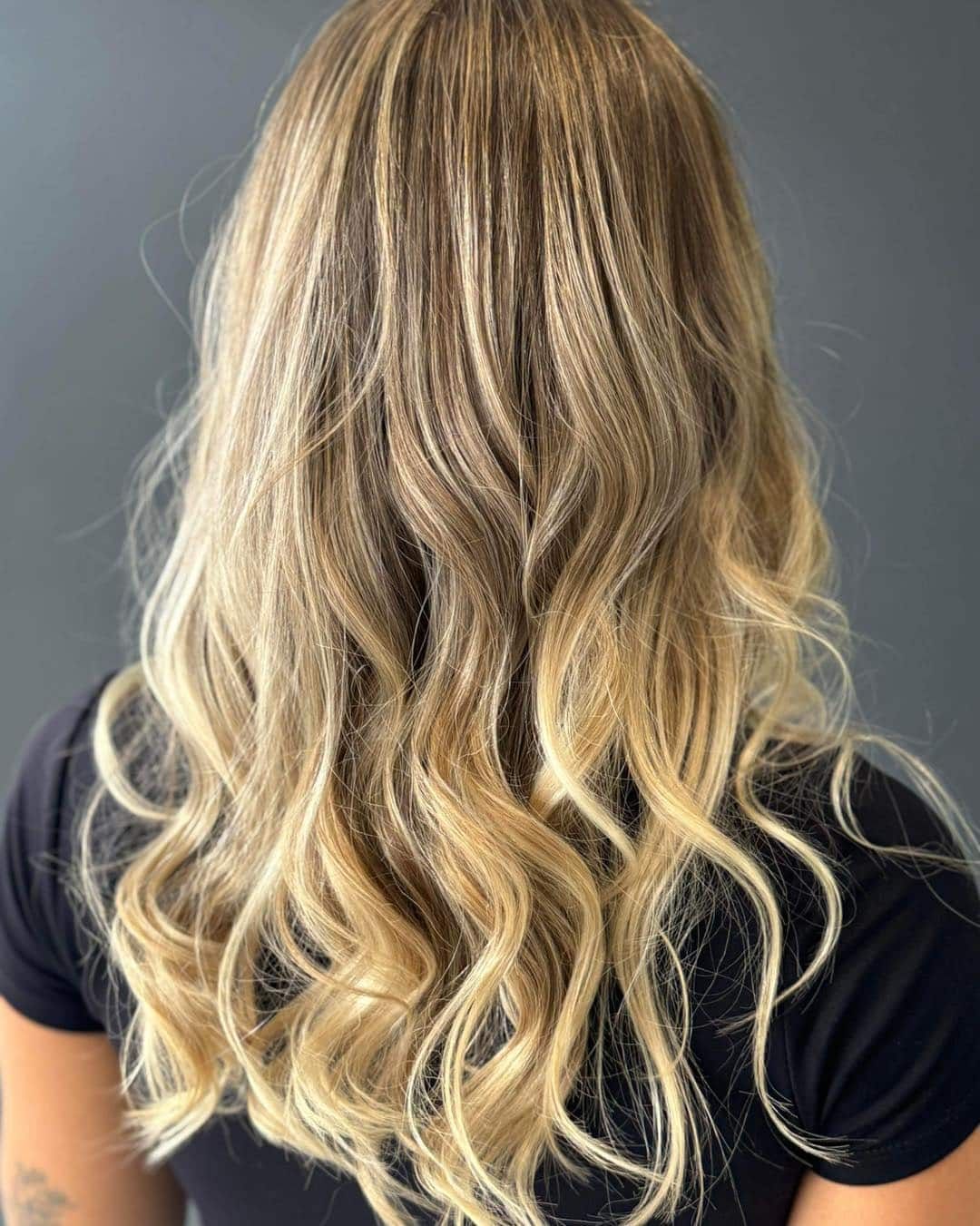 A Woman With Long Blonde Hair is Wearing a Black Shirt — Glam Hair and Beauty in Woy Woy, NSW