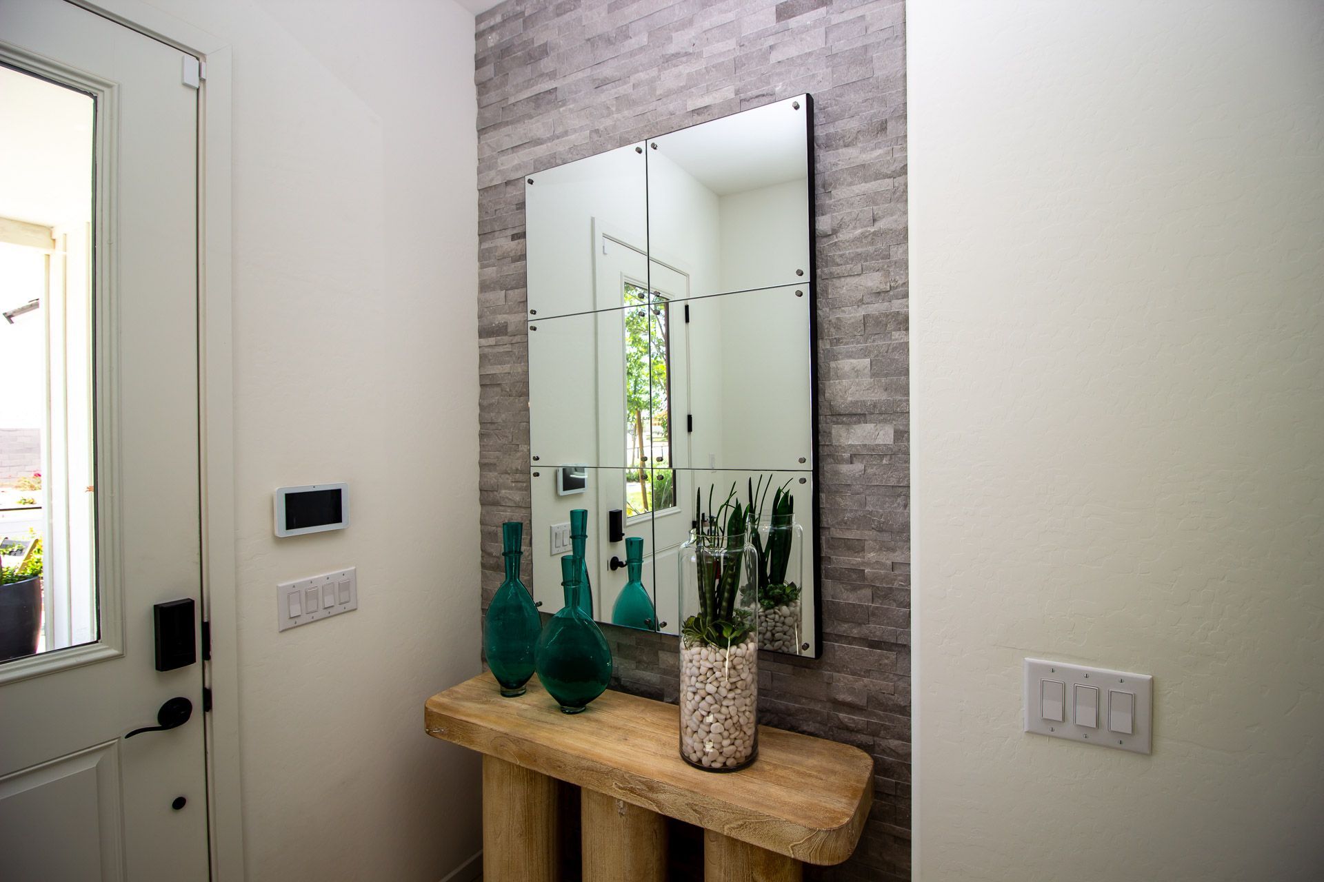 Entryway with a wooden console table, mirror, green vases, and a potted plant against a light wall.