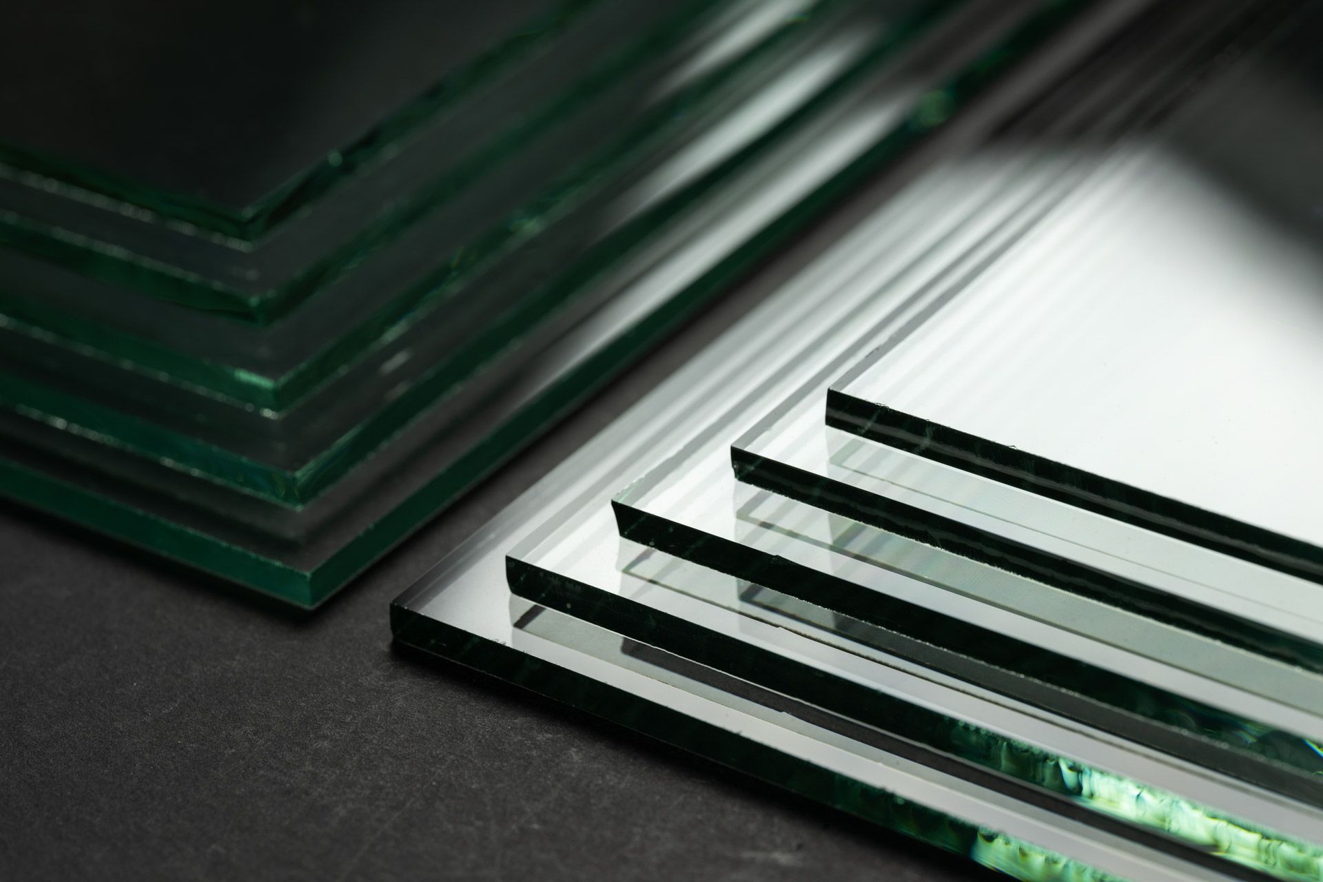 Stacked green-tinted glass sheets on a dark surface, with several narrow glass strips in the foreground.