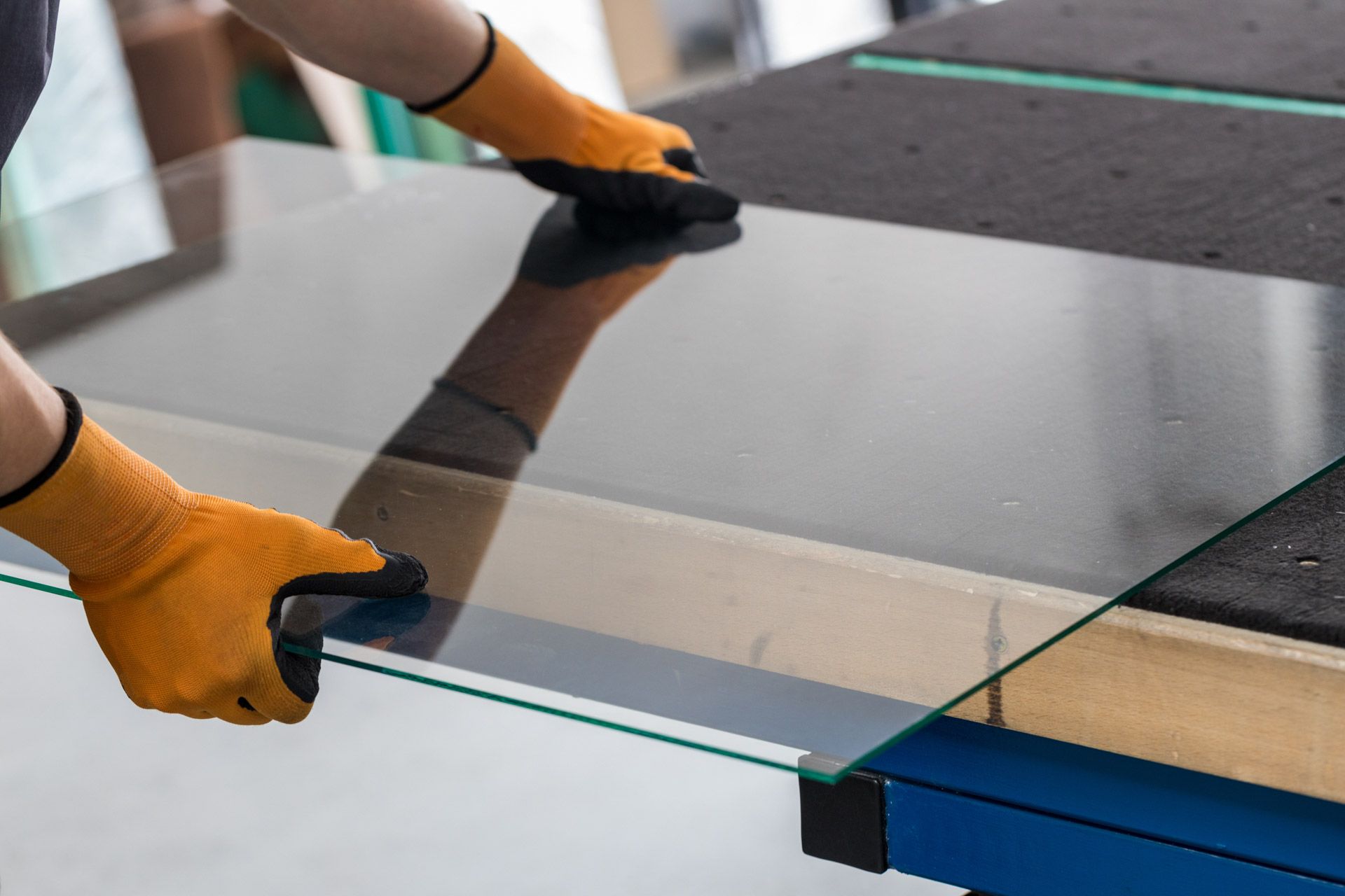 Gloved hands handling a clear glass panel on a worktable