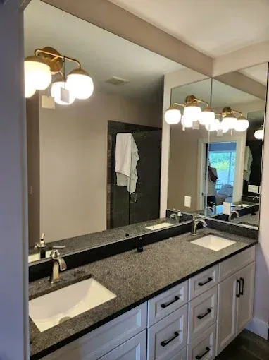 Modern bathroom vanity with dual sinks, large mirror, granite countertop, and brass light fixtures