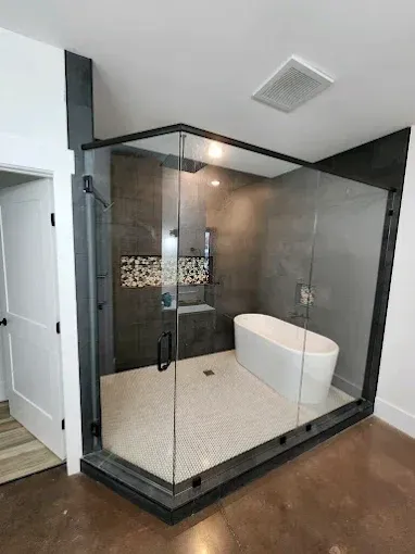 Modern glass shower enclosure with freestanding white bathtub and light tile flooring in a bathroom