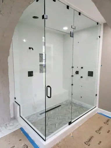 Glass walk-in shower with black fixtures and gray tile floor in a bright bathroom