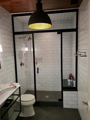 Modern bathroom with black-framed glass shower, white subway tile, toilet, and pendant light