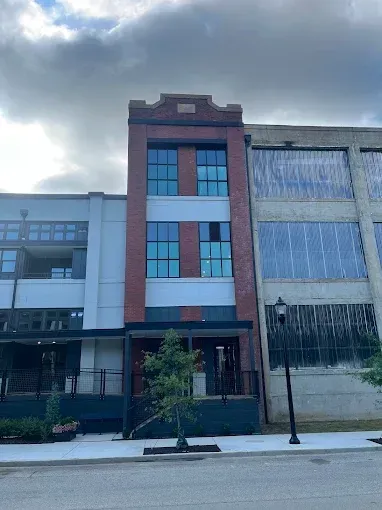 Tall narrow brick building with blue windows and a sidewalk under cloudy sky