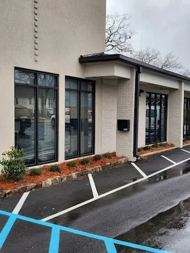Wet exterior of a beige building with black-framed windows and blue-striped parking spaces.