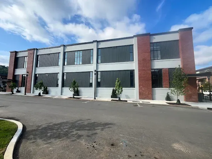 Modern two-story office building with red brick and gray panels beside an empty paved lot