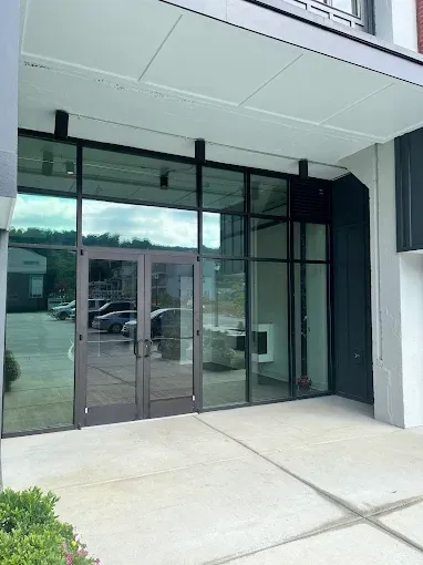 Glass storefront entrance with black framing and concrete sidewalk under an overhang