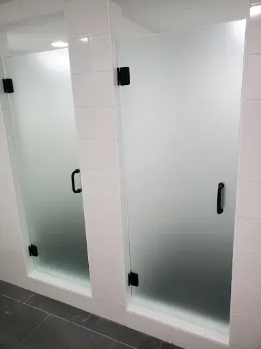 Two frosted glass restroom stall doors with black handles in a tiled bathroom
