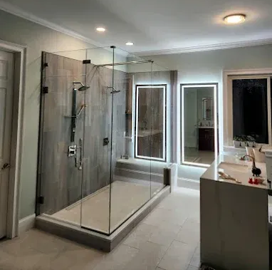 Modern bathroom with a glass walk-in shower, double vanity, and bright mirrored lighting