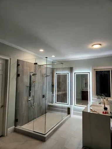 Modern bathroom with glass-enclosed shower, large mirror, vanity, and recessed ceiling lights.