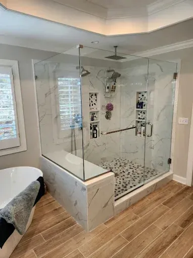 Glass walk-in shower with tile floor and bench in a bright bathroom