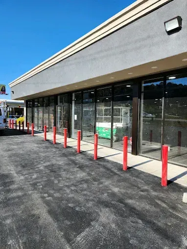 Storefront with glass windows, red bollards, and paved parking lot under a beige awning