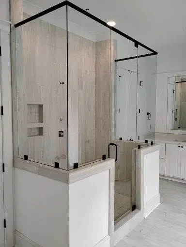 Small glass shower enclosure with black trim and light wood panels in a white bathroom.