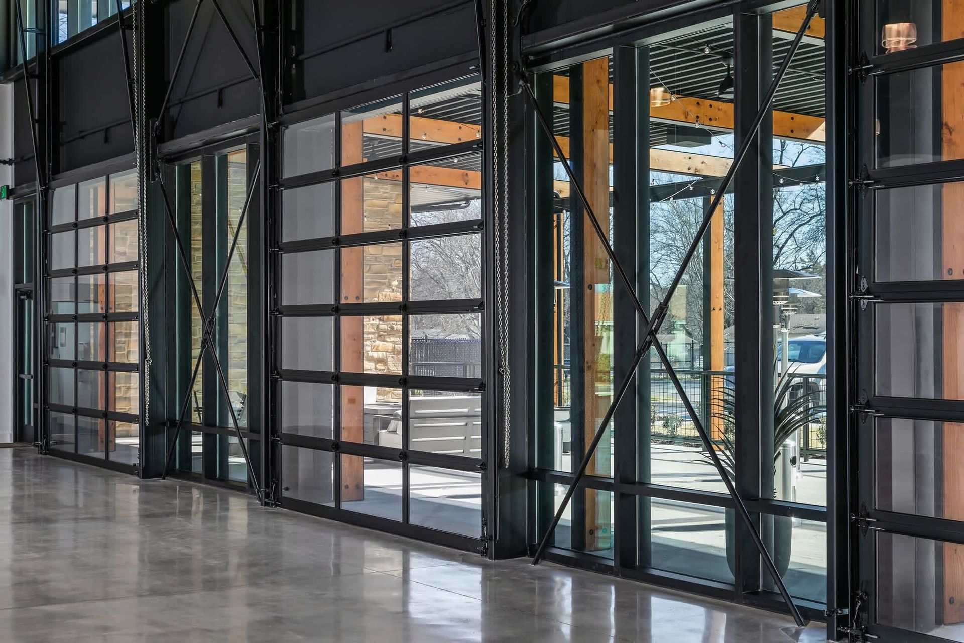 Empty modern lobby with floor-to-ceiling glass doors, black metal frames, and polished concrete floor