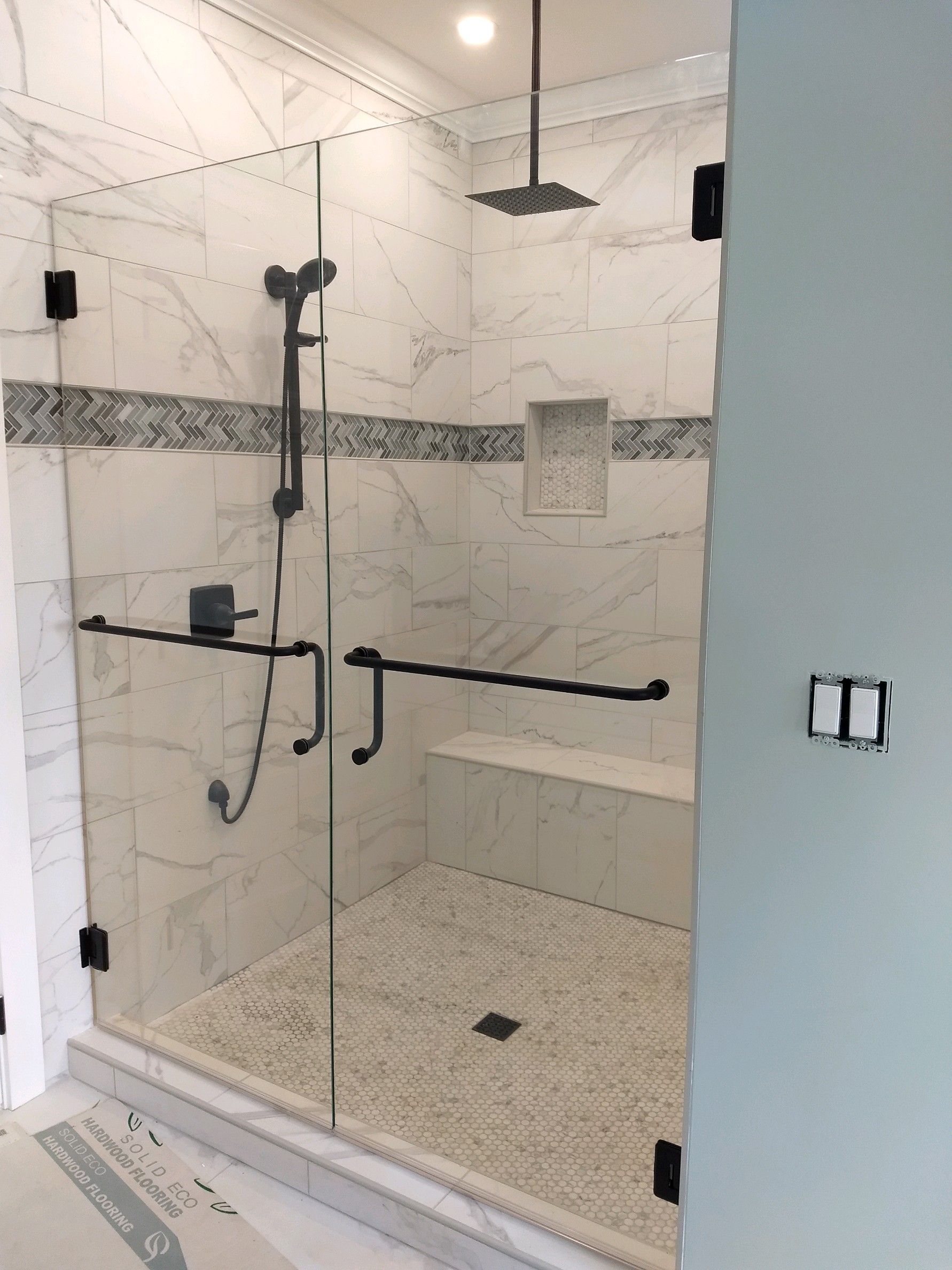 Walk-in shower with bench, grab bars, handheld showerhead, and marble tile walls