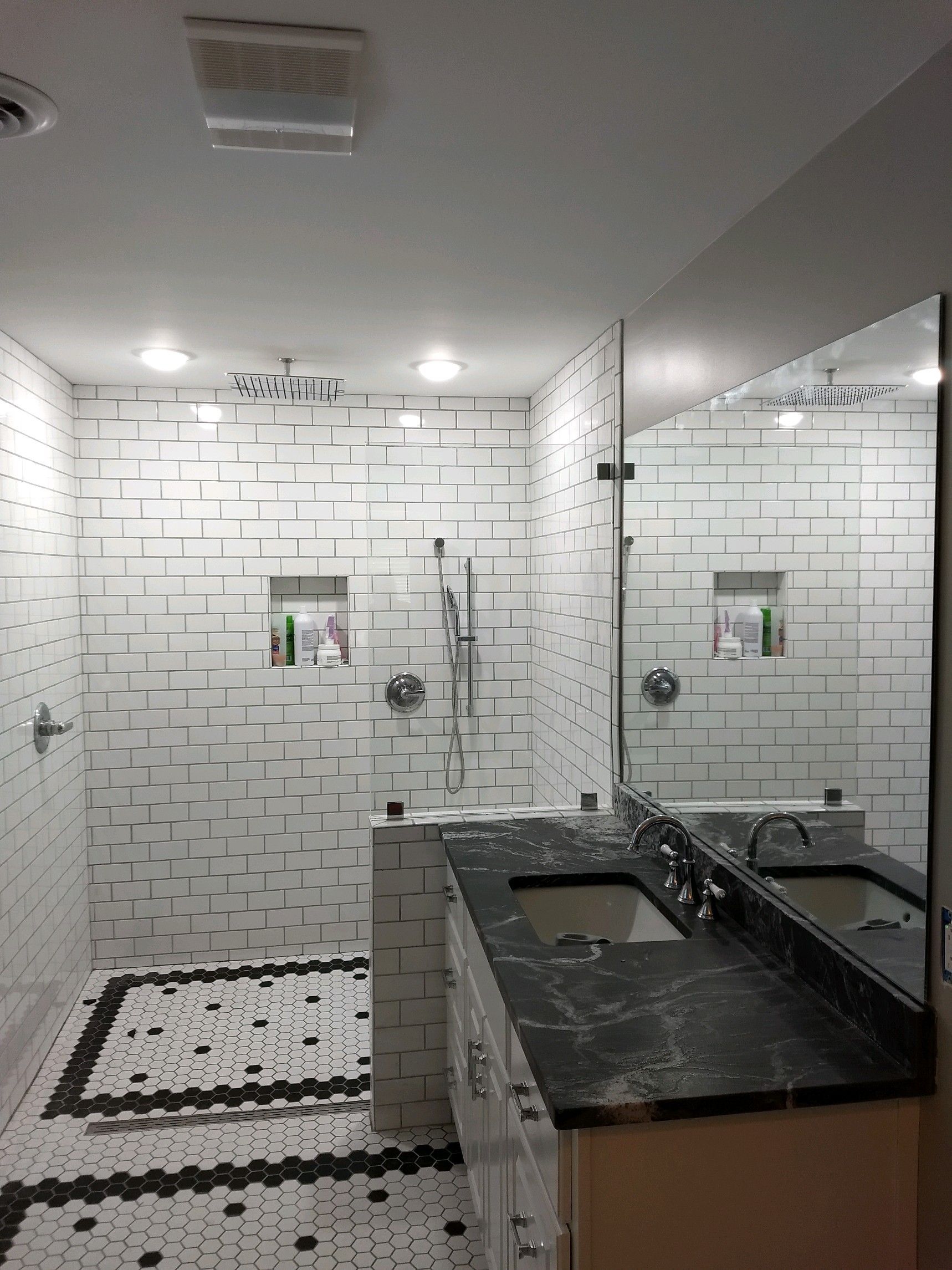 Modern bathroom with white tiled shower, black countertop, and large mirror, bright and clean.