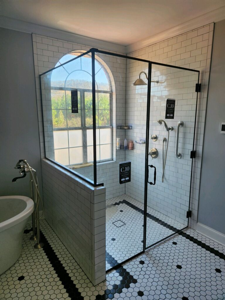 Modern black-framed glass shower with white tile, built-in bench, and windowed bathroom view